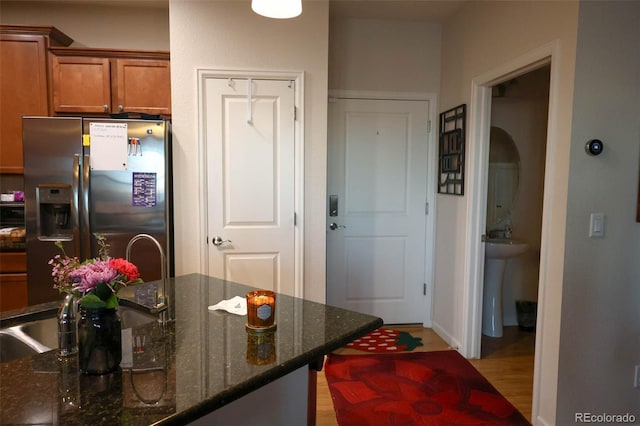 kitchen with light wood finished floors, dark stone counters, arched walkways, stainless steel refrigerator with ice dispenser, and brown cabinets