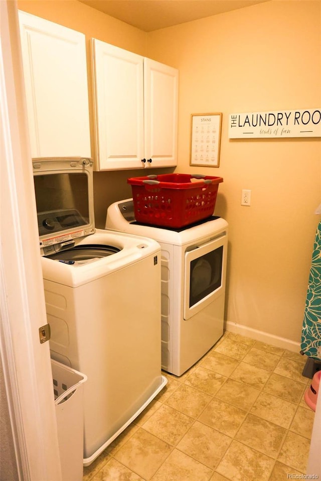 clothes washing area featuring washing machine and dryer, cabinet space, and baseboards