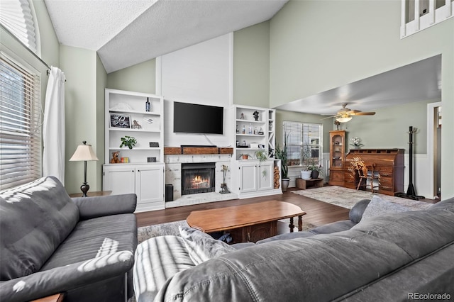 living room with built in shelves, wood-type flooring, high vaulted ceiling, a textured ceiling, and ceiling fan