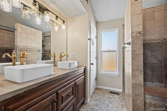 bathroom with tiled shower, vanity, and a textured ceiling