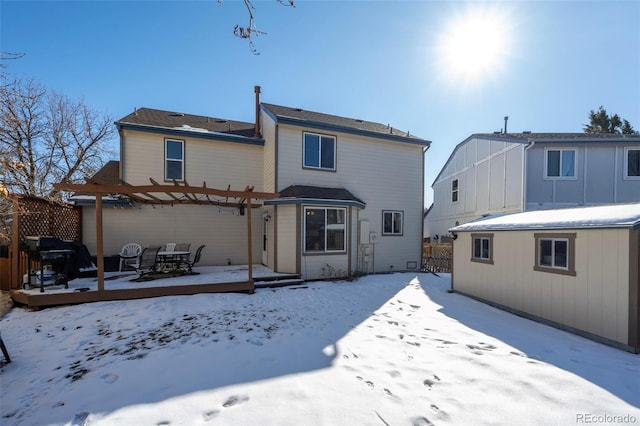 snow covered house with a wooden deck, an outbuilding, and a pergola