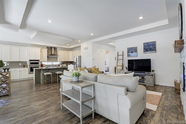 living area featuring a tray ceiling, recessed lighting, dark wood-type flooring, and baseboards