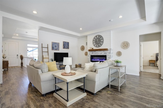 living room with a tray ceiling, dark wood-style flooring, recessed lighting, a glass covered fireplace, and baseboards
