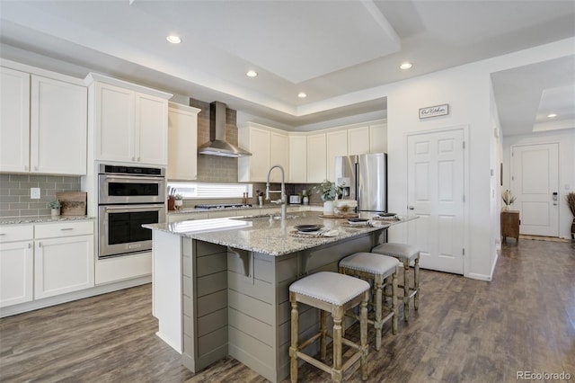 kitchen featuring wall chimney exhaust hood, a sink, recessed lighting, appliances with stainless steel finishes, and dark wood-style floors