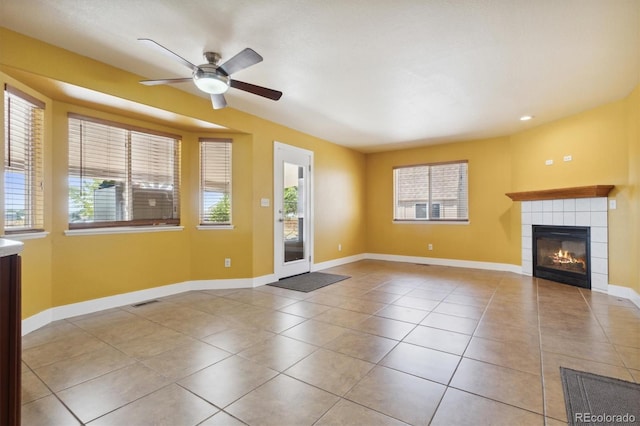 unfurnished living room featuring a tiled fireplace, plenty of natural light, light tile patterned floors, and ceiling fan