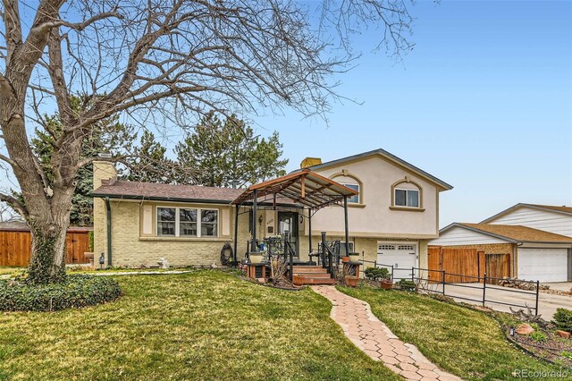 split level home featuring a chimney, an attached garage, fence, brick siding, and a front lawn