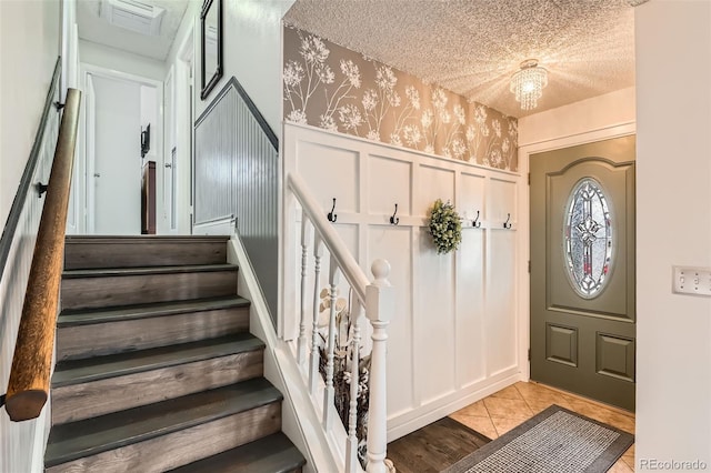 entrance foyer featuring light tile patterned flooring, a textured ceiling, wallpapered walls, and stairway