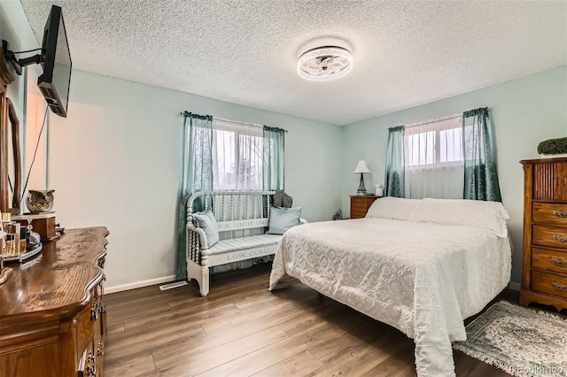 bedroom with baseboards, a textured ceiling, and wood finished floors