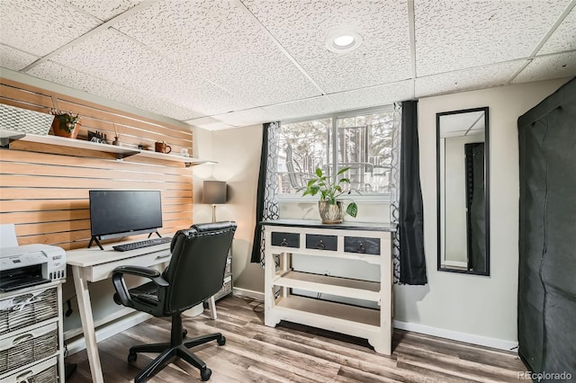 office area featuring baseboards, wood finished floors, and a paneled ceiling