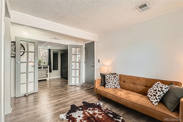 living area with visible vents, wood finished floors, french doors, and a textured ceiling