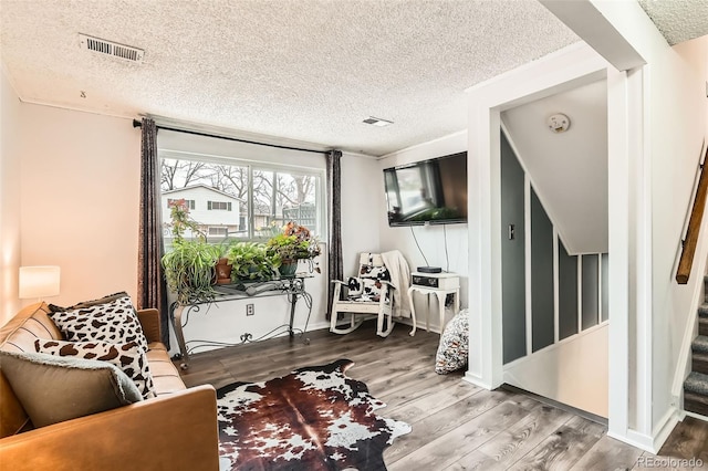 living area with visible vents, wood finished floors, stairway, and a textured ceiling