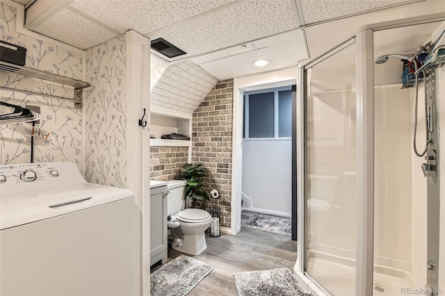 full bath featuring washer / clothes dryer, wood finished floors, toilet, wallpapered walls, and a stall shower
