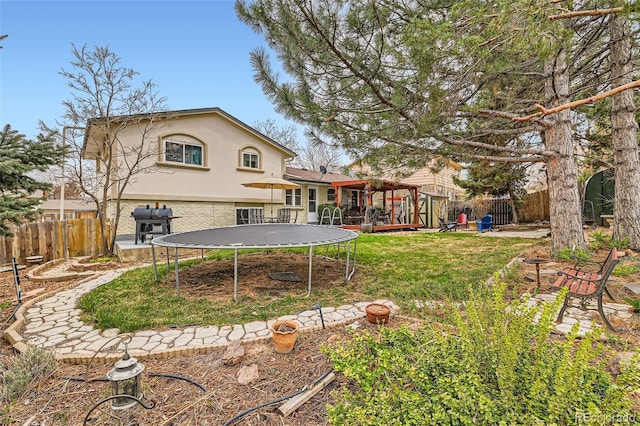 back of house with a trampoline, a fenced backyard, stucco siding, and a yard