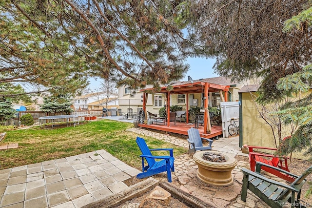 view of yard with fence, a wooden deck, a trampoline, a fire pit, and a patio area