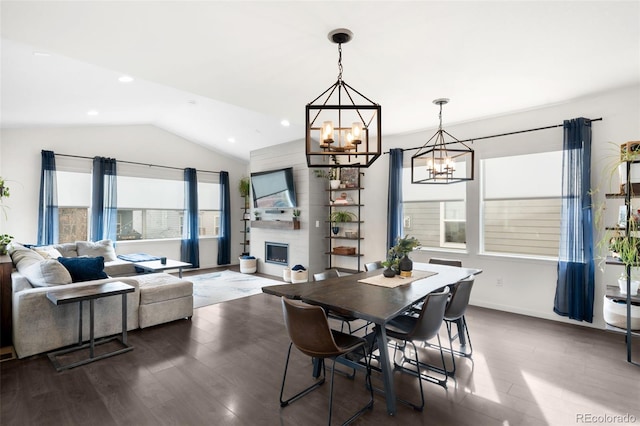 dining area with a large fireplace, a healthy amount of sunlight, dark wood-type flooring, and vaulted ceiling