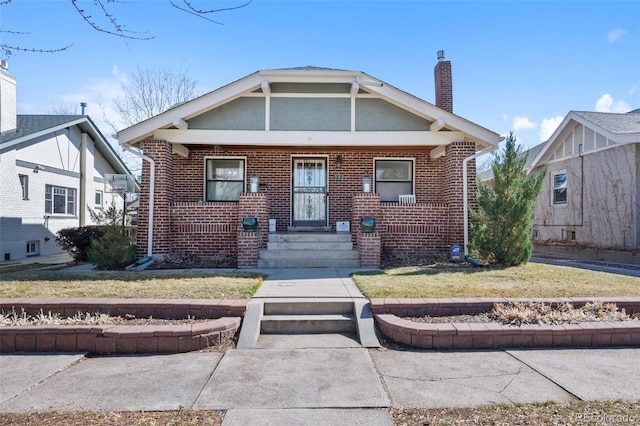 bungalow-style house with brick siding, a chimney, and a front lawn