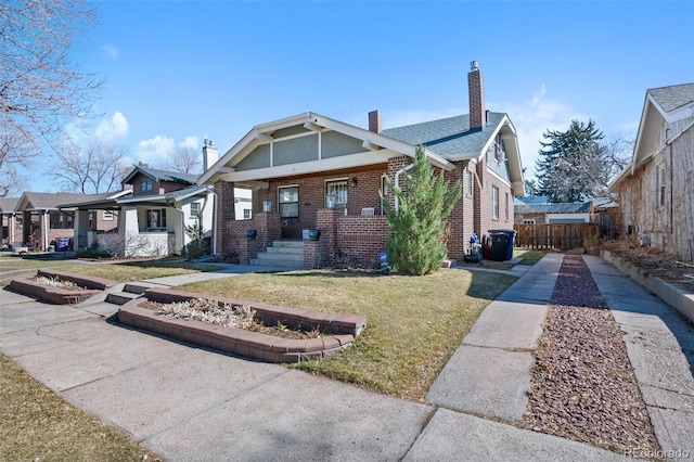 bungalow-style house with a front yard, brick siding, fence, and a chimney