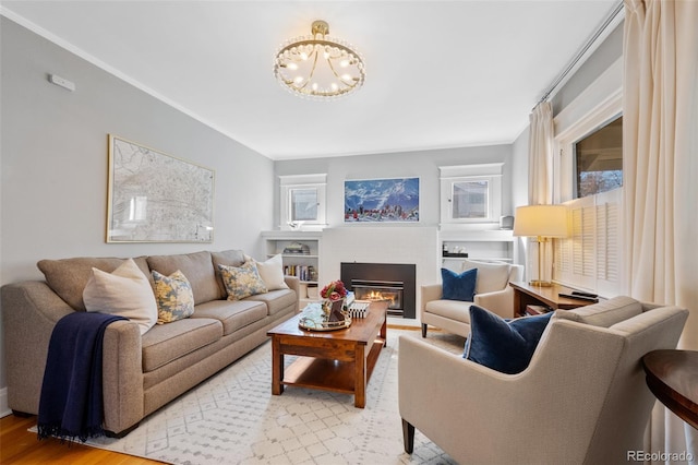 living area featuring a chandelier, light wood-type flooring, plenty of natural light, and a glass covered fireplace