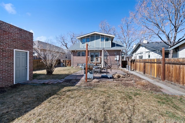 rear view of house with a yard, a patio, brick siding, and a fenced backyard