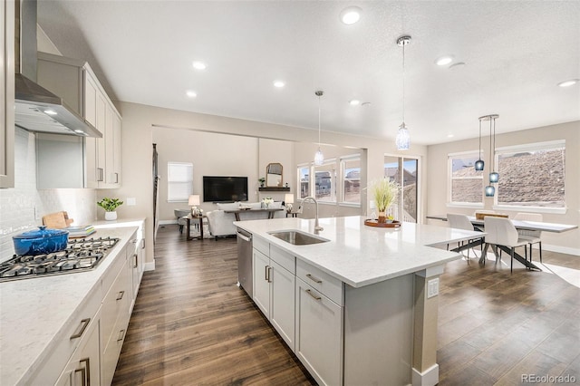 kitchen with dark wood finished floors, stainless steel appliances, decorative backsplash, a sink, and wall chimney exhaust hood