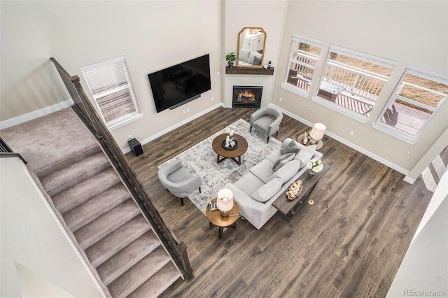 living room with stairs, a glass covered fireplace, wood finished floors, and baseboards