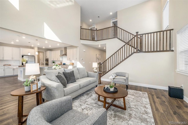 living area featuring visible vents, dark wood-style flooring, a high ceiling, baseboards, and stairs