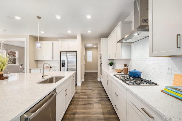 kitchen featuring dark wood-style flooring, stainless steel appliances, hanging light fixtures, a sink, and wall chimney exhaust hood