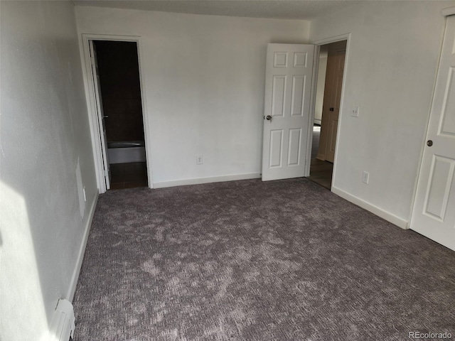 unfurnished bedroom featuring dark colored carpet, a baseboard heating unit, and ensuite bath