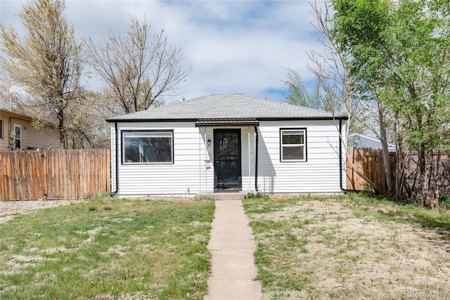 bungalow featuring fence, roof with shingles, and a front lawn