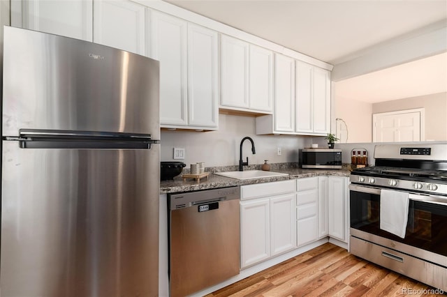 kitchen featuring a sink, light wood finished floors, dark stone counters, stainless steel appliances, and white cabinetry