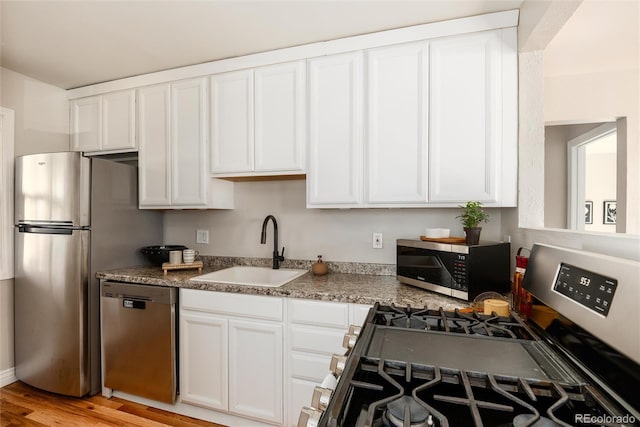 kitchen featuring stainless steel appliances, white cabinetry, a sink, and light wood-style flooring
