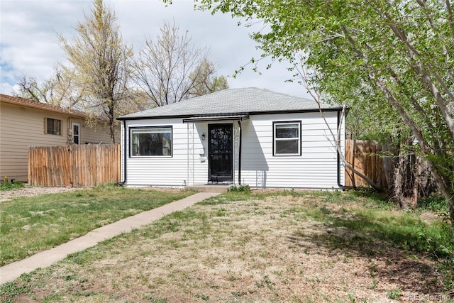 bungalow-style home with a shingled roof, a front lawn, and fence