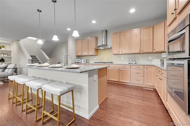 20145 E Fair Ln, Centennial, CO 80016 - kitchen featuring light brown cabinets, wall chimney exhaust hood, wood finished floors, appliances with stainless steel finishes, and a breakfast bar