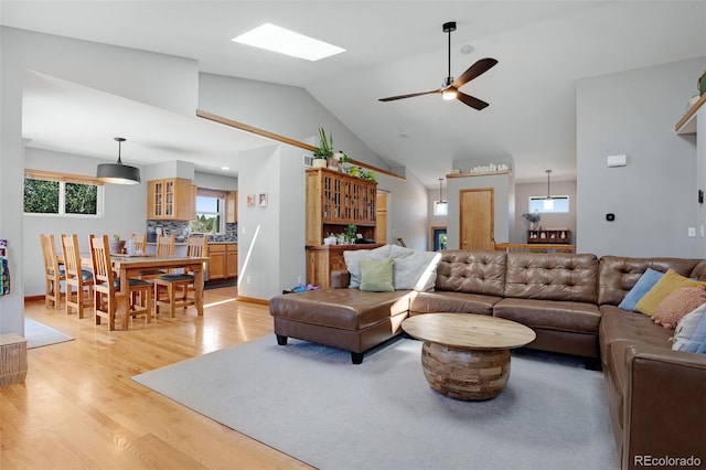 living room featuring ceiling fan, vaulted ceiling with skylight, and light hardwood / wood-style floors