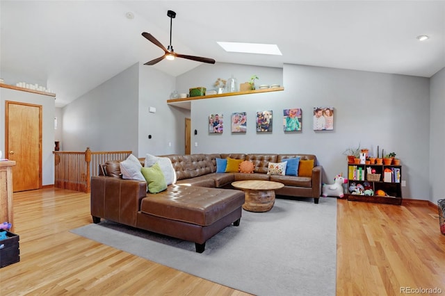 living room featuring ceiling fan, light wood-type flooring, and vaulted ceiling with skylight