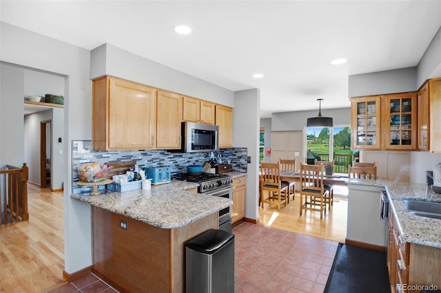 kitchen featuring light wood-type flooring, kitchen peninsula, appliances with stainless steel finishes, and light stone counters