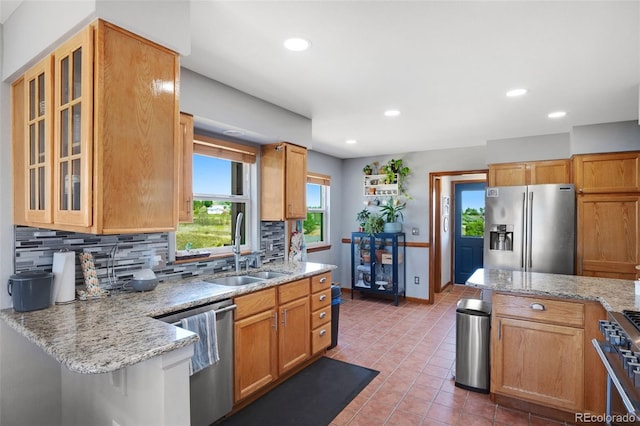 kitchen featuring appliances with stainless steel finishes, light stone countertops, backsplash, tile patterned floors, and sink