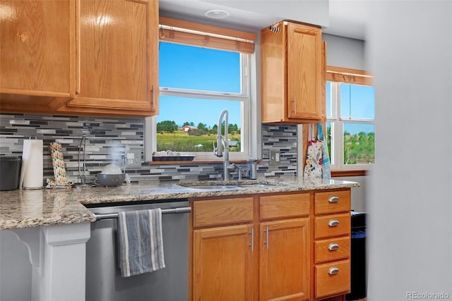 kitchen with sink, stainless steel dishwasher, backsplash, and light stone countertops