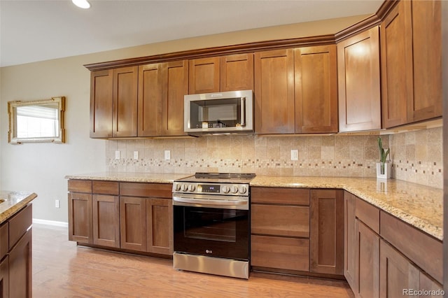 4784 Raven Run, Broomfield, CO 80023 - kitchen with brown cabinets, light stone counters, light wood finished floors, backsplash, and stainless steel appliances
