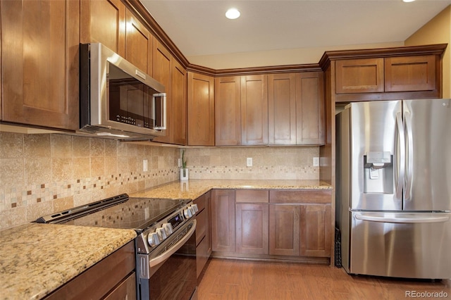4784 Raven Run, Broomfield, CO 80023 - kitchen with appliances with stainless steel finishes, decorative backsplash, brown cabinetry, and light wood finished floors