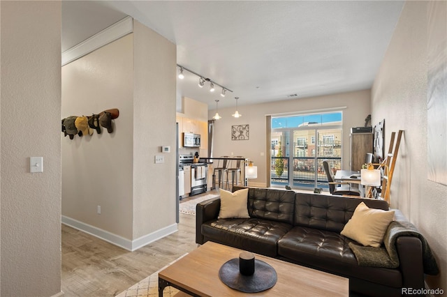 living room with light wood finished floors, visible vents, baseboards, a textured wall, and rail lighting