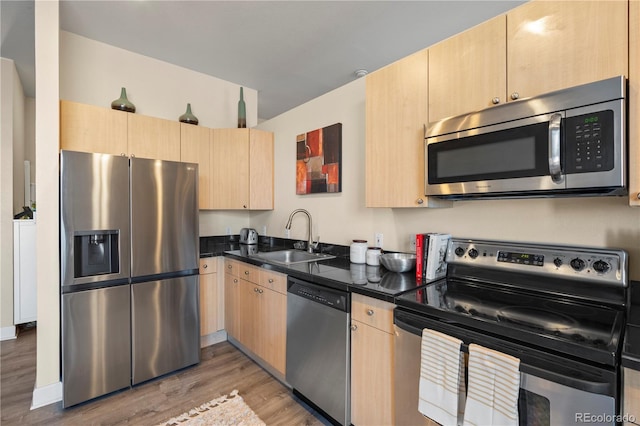 kitchen featuring light brown cabinets, appliances with stainless steel finishes, dark countertops, and a sink