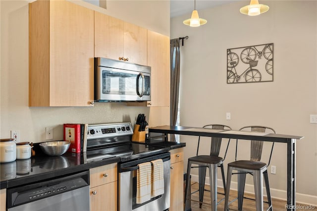 kitchen featuring baseboards, dark countertops, stainless steel appliances, light brown cabinets, and pendant lighting