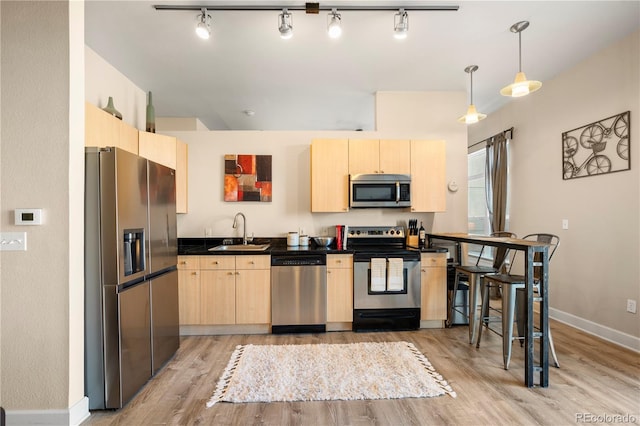 kitchen featuring dark countertops, appliances with stainless steel finishes, a sink, and light brown cabinetry