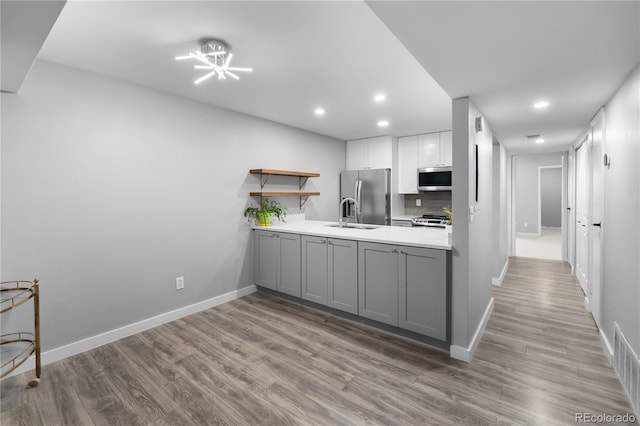 kitchen with gray cabinetry, white cabinetry, stainless steel appliances, and light hardwood / wood-style flooring