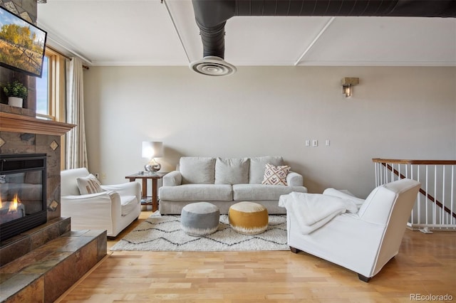 living room featuring a tiled fireplace, crown molding, and light hardwood / wood-style floors