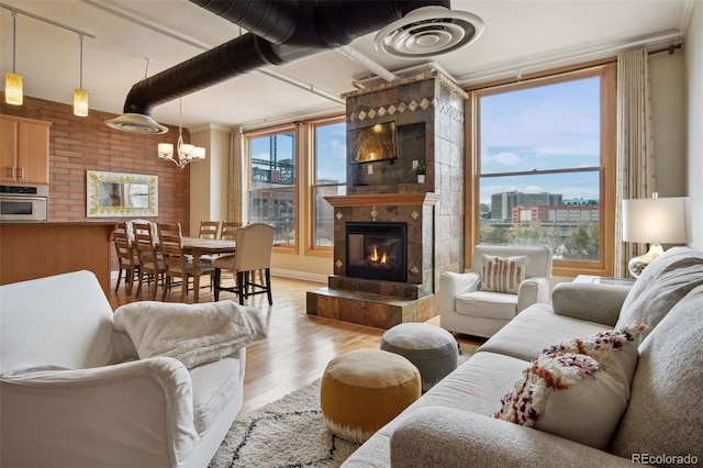 living room featuring a tiled fireplace, brick wall, a notable chandelier, and light hardwood / wood-style flooring