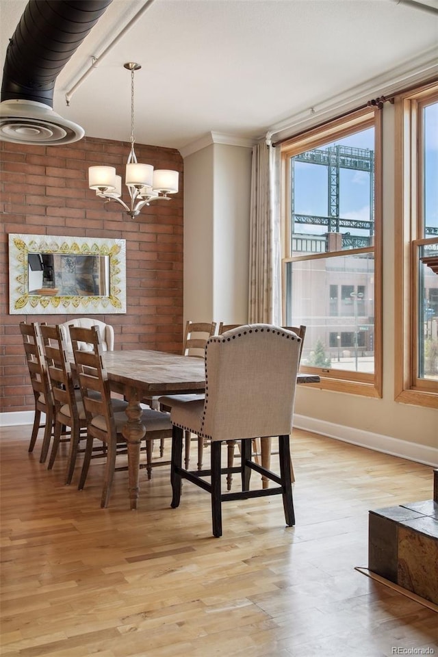 dining area with a notable chandelier, crown molding, brick wall, and light wood-type flooring