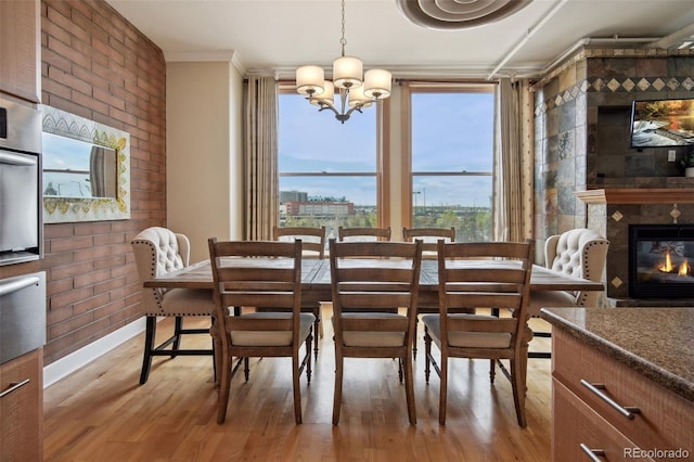 dining room featuring a fireplace, ornamental molding, brick wall, a chandelier, and light wood-type flooring