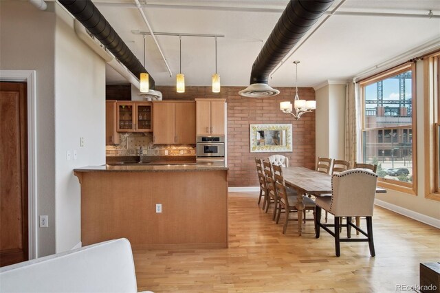 kitchen with pendant lighting, an inviting chandelier, kitchen peninsula, oven, and light wood-type flooring